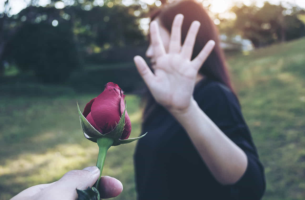 公園で深紅のバラを一輪差し出す男性の手を左の掌を見せて拒否する女性