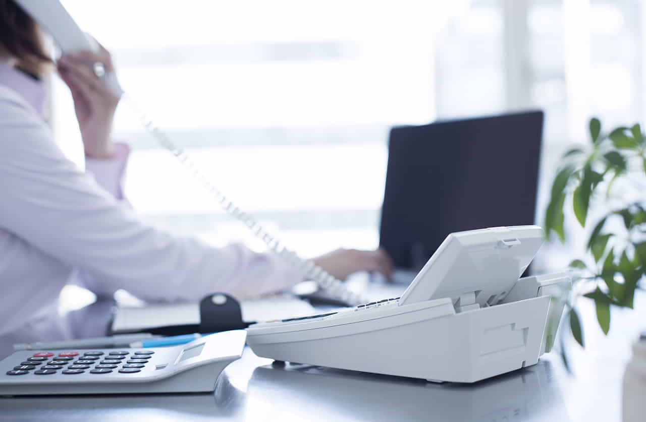 デスクでパソコンを操りながら電話をする女性