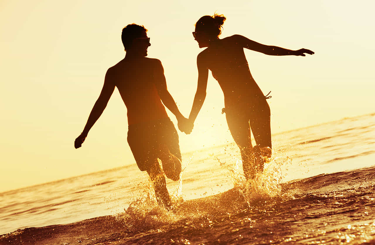 夕日に染まる海辺で手をつなぎ笑い合いながらはしゃぐ恋人